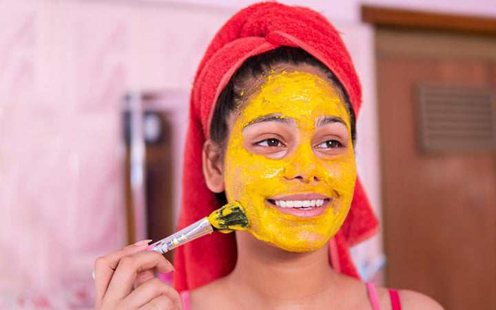 Mooi meisje dat kurkuma geel gezichtsmasker op gezicht aanbrengt door borstel