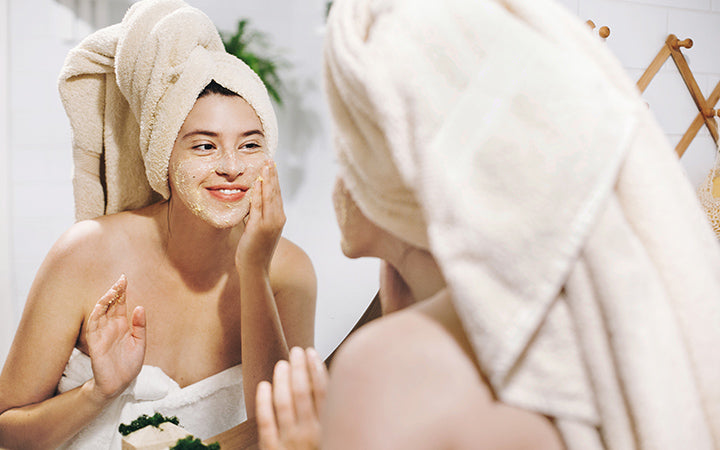 Gelukkige vrouw in handdoek die gezichtsmassage maakt met organische gezichtsscrub