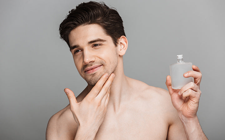 Schoonheid portret van knappe jonge man met behulp van aftershave lotion