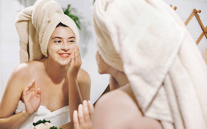 Jonge gelukkige vrouw in handdoek die gezichtsmassage maakt met organische gezichtsscrub