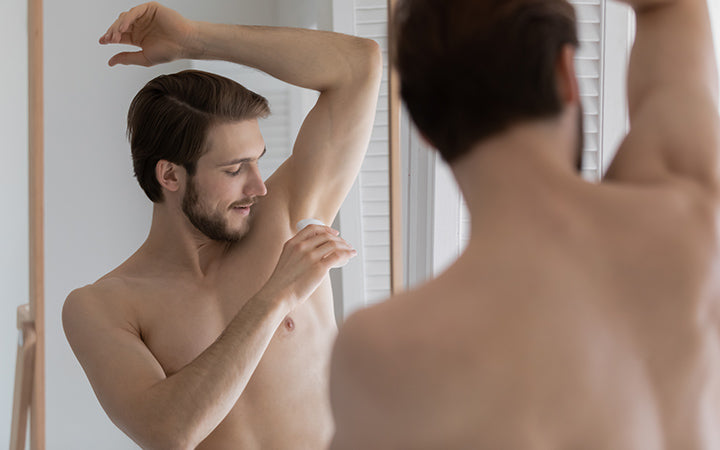 spiegelreflectie jongeman die anti-transpirant op oksel aanbrengt na het douchen